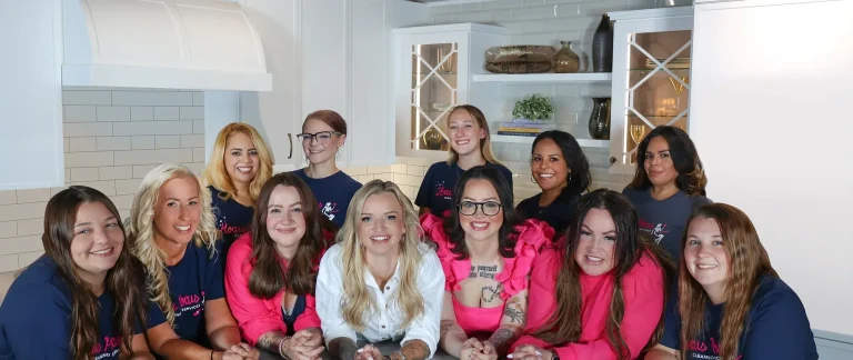 A group photo of the Hocus Pocus Cleaning Services team smiling in a bright, modern kitchen. The team members are wearing navy blue and bright pink branded shirts, representing the brand's unique cleaning niche.